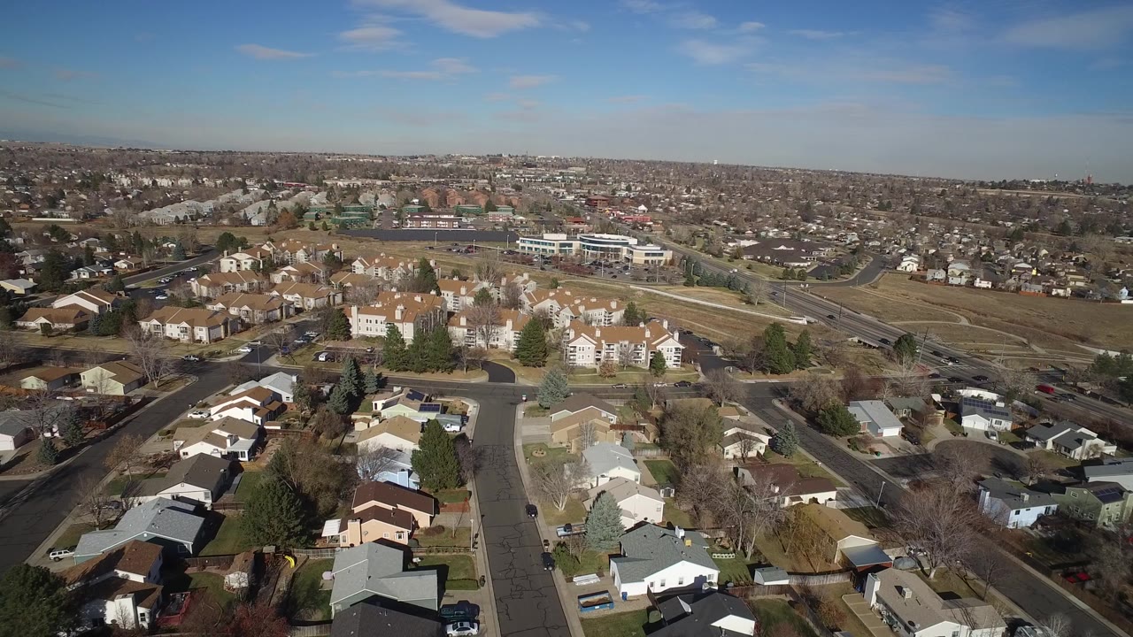High view of suburban homes beside roads and undeveloped land beneath a clear sky.