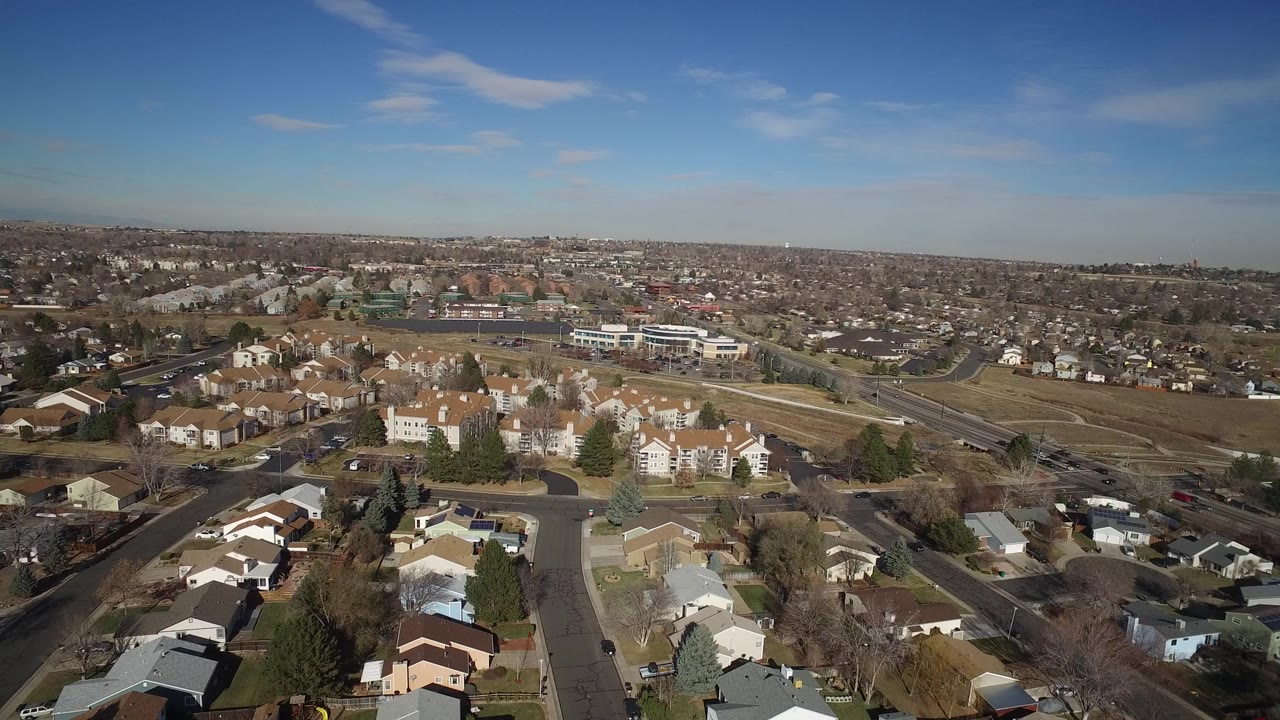 Aerial view of suburban houses, streets, trees, and a wide blue sky.