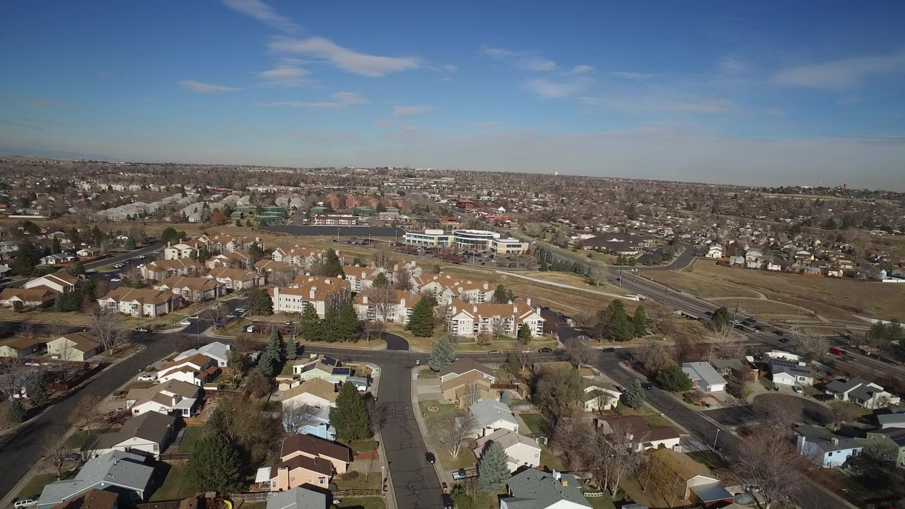 Aerial view over Hidden Lake, Colorado, with clustered homes in the foreground, larger residential buildings near the center, roadways, open brown ground, and no visible people.