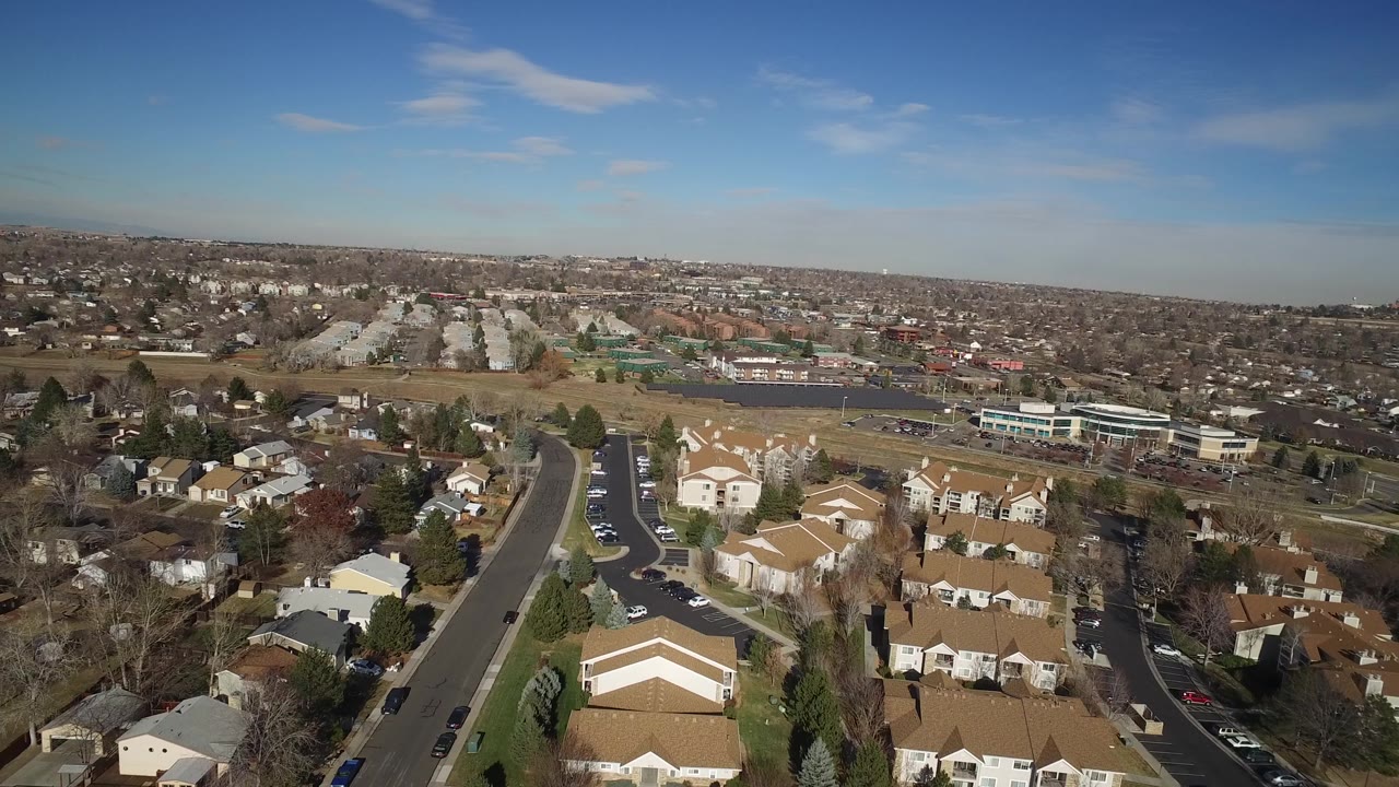 The second frame shows Hidden Lake rooftops and a straight residential road in the foreground, with brown fields, low buildings, distant homes, and no visible people.