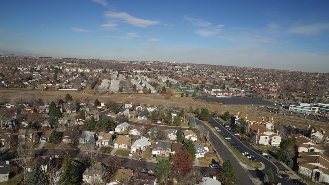High view across rooftops, a curved road, fields, and suburban development.