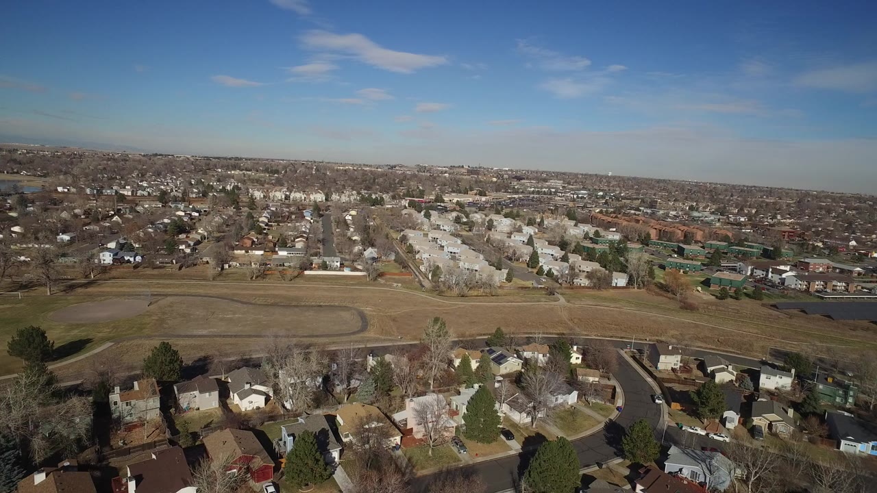 Aerial view of suburban homes beside a broad open field under blue sky.