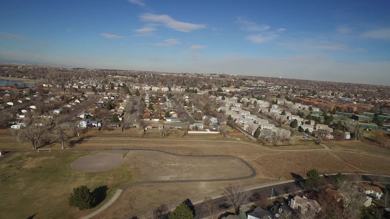 Aerial view of a park field, homes, and distant water under a blue sky.