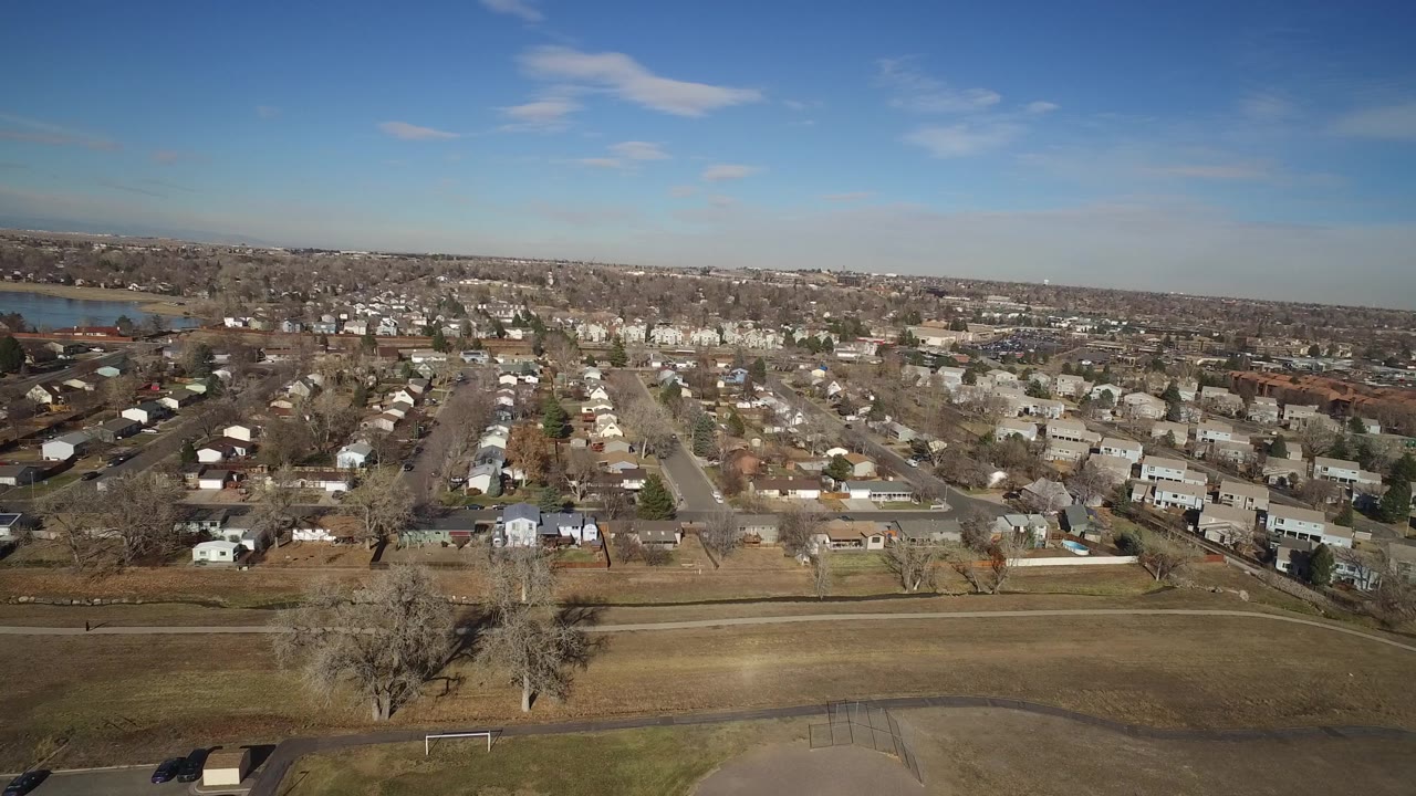 Elevated view of homes and streets beyond a brown open field under blue sky.