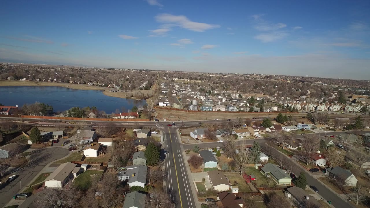 Aerial view of lake, suburban homes, roads, and blue sky.