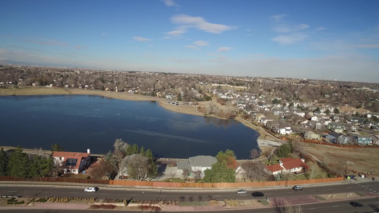 Aerial view of a lake beside suburban homes and a road