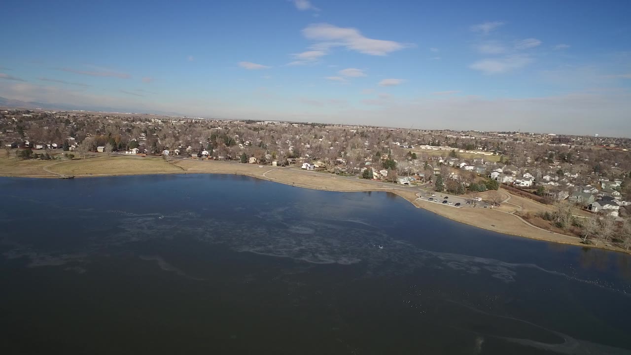 Aerial view of lake shoreline and residential town under blue sky.
