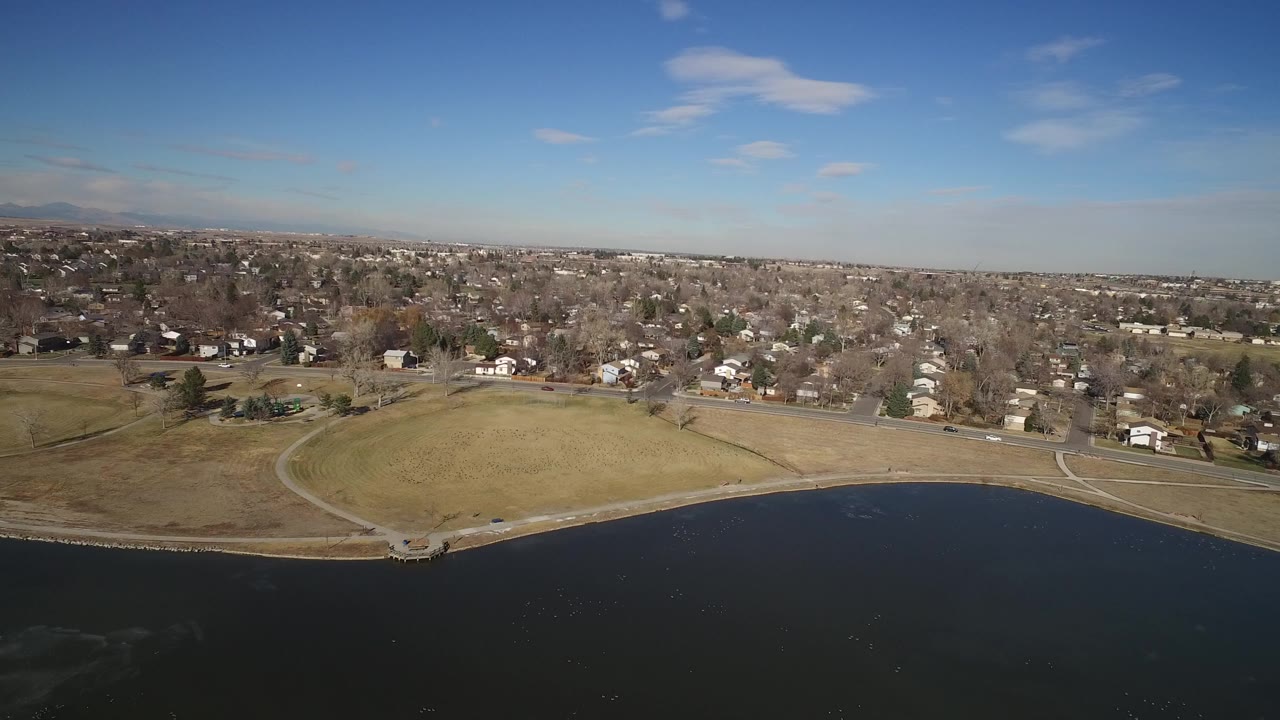Aerial view of lake water, curved park shoreline, open grass, and residential neighborhood.