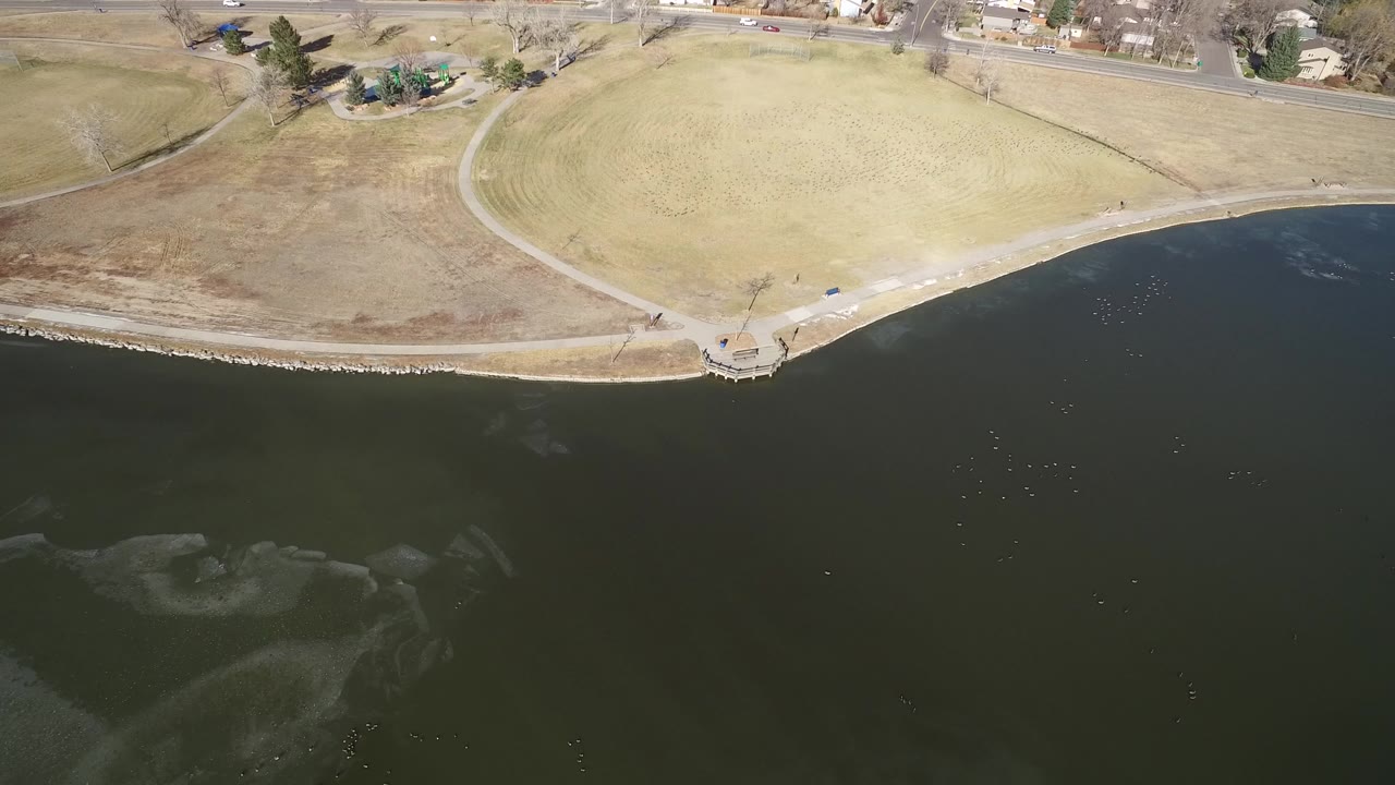 Aerial view of lake water beside a curving park path and open grass.