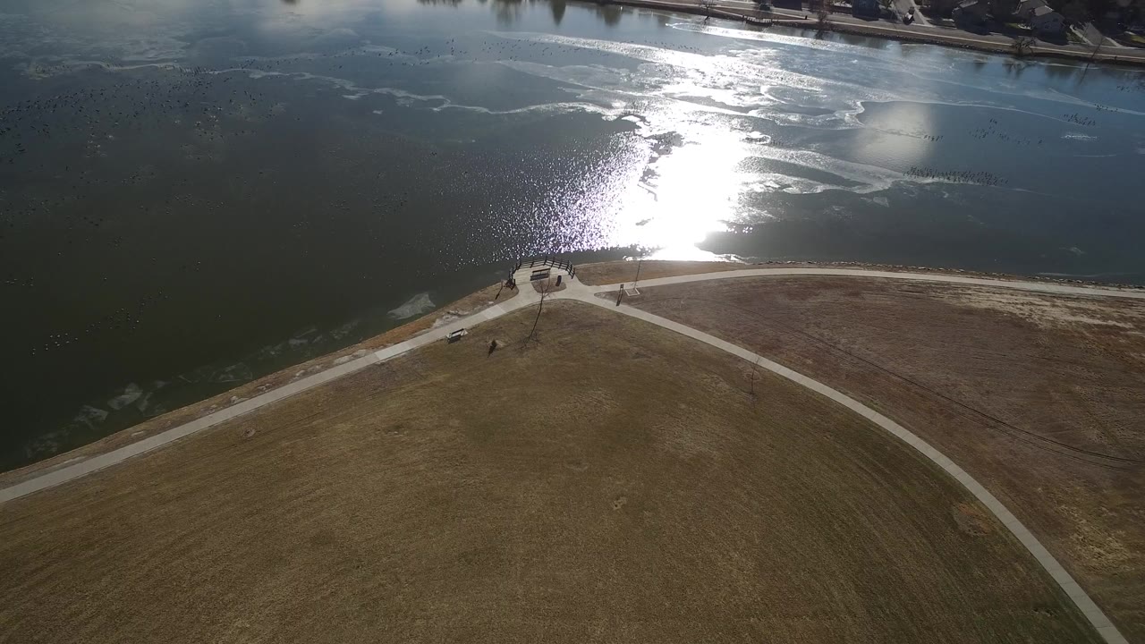 Aerial view of lake water, shoreline path, and open field in bright sun.