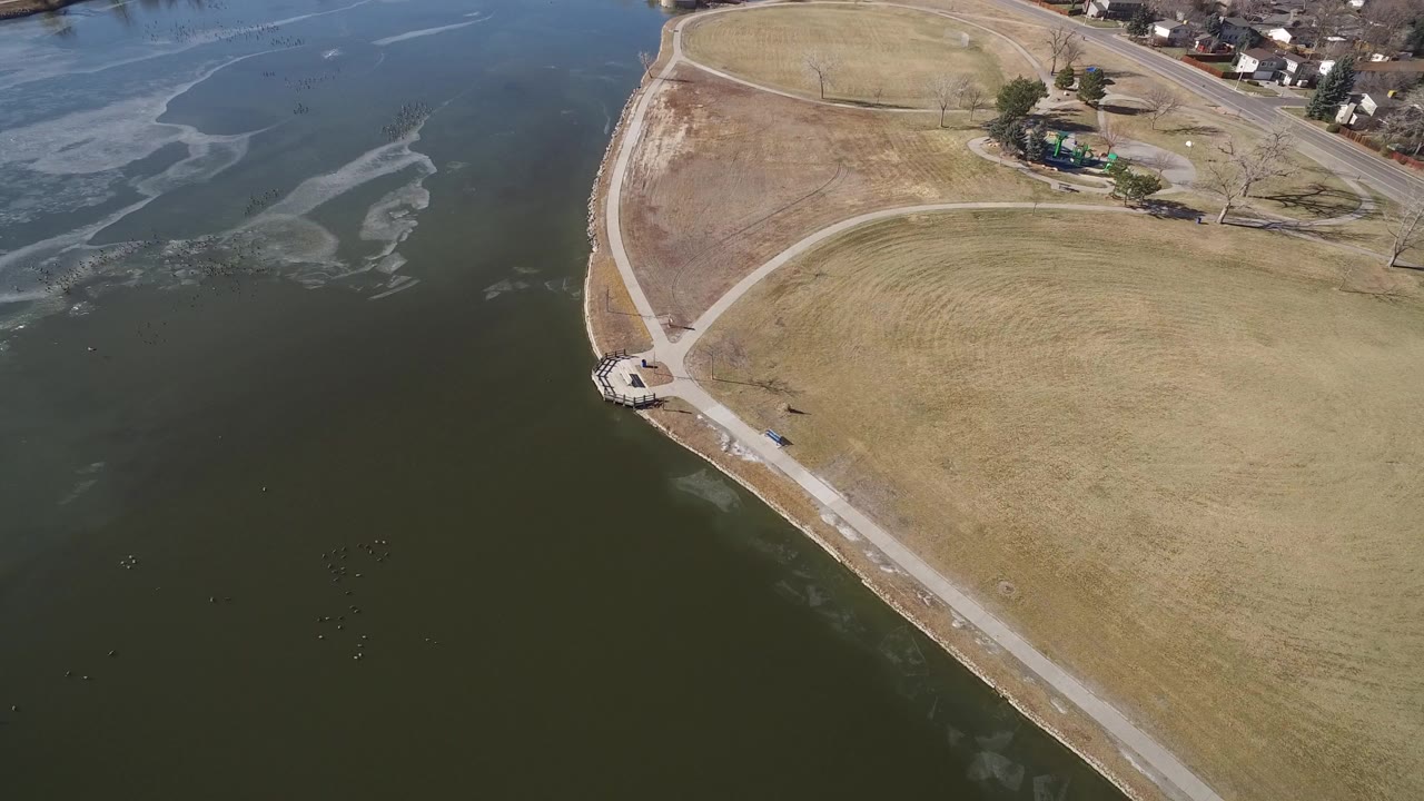Aerial view of a curved lake shoreline beside open grass and paths.