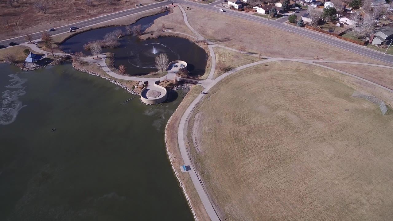 Aerial view of a lake, circular pond, paths, road, and homes.
