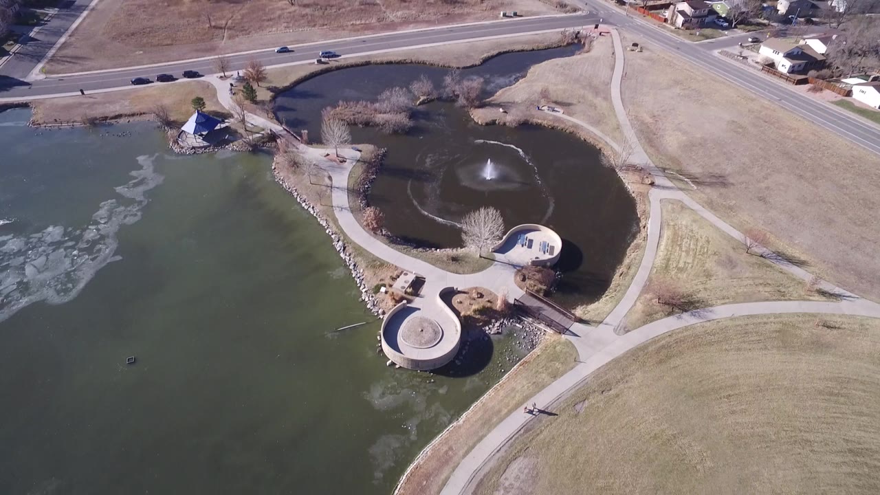 Overhead Hidden Lake, Colorado frame with the large pond on the left, the smaller dark pond and fountain at upper right, pale water surface patterns, roads, lawns, and no visible people.