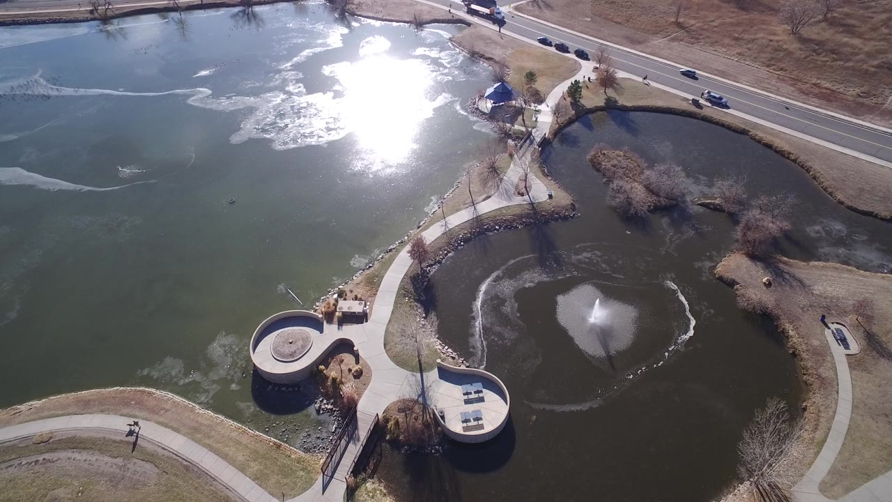 Aerial view of park lakes, a fountain pond, curved paths, and a road.