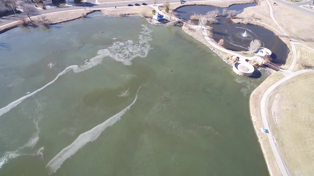 Aerial view of a partly frozen lake beside curved paths and a road.