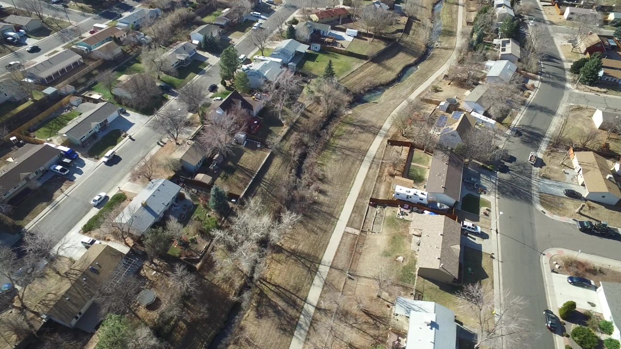Overhead view of suburban homes, streets, sidewalks, bare trees, and parked cars.