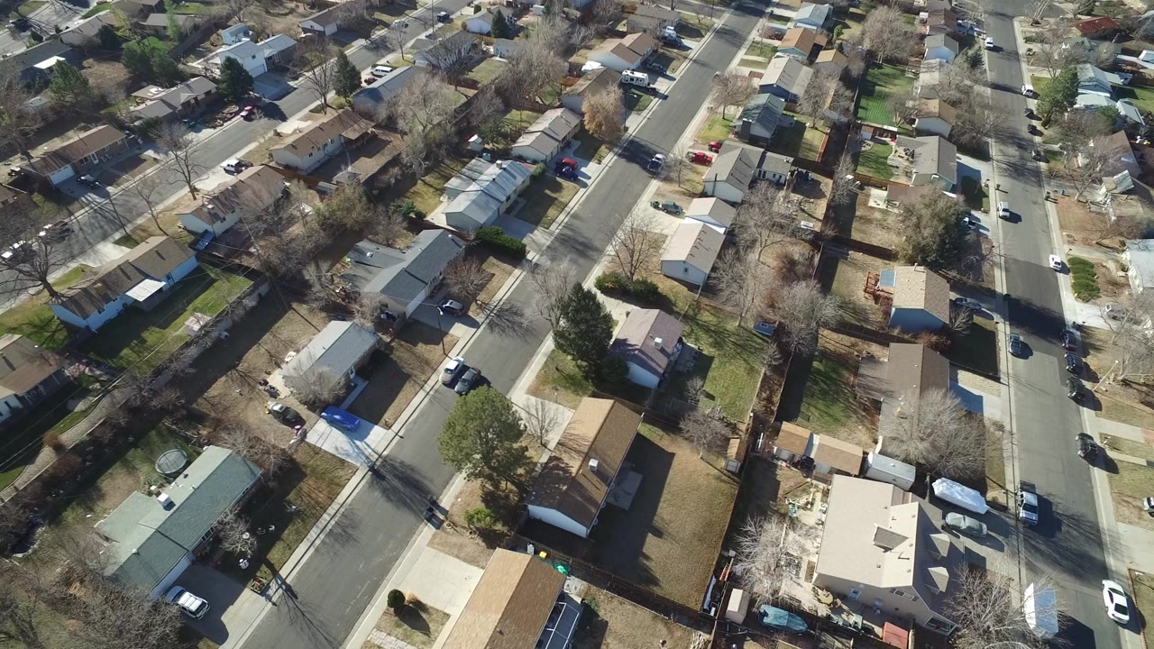 Aerial view over Hidden Lake, Colorado residential blocks with single-story houses, fenced yards, leafless trees, parked vehicles, and no visible people.