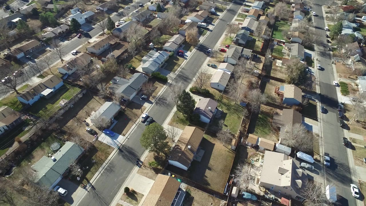 Drone view over Hidden Lake, Colorado homes and yards, with a white car on the right-side street and no visible people.