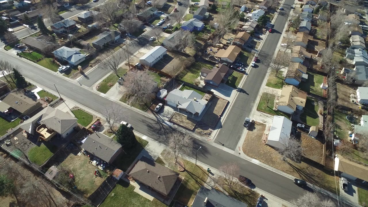 Aerial view of residential streets, houses, yards, trees, and parked vehicles.