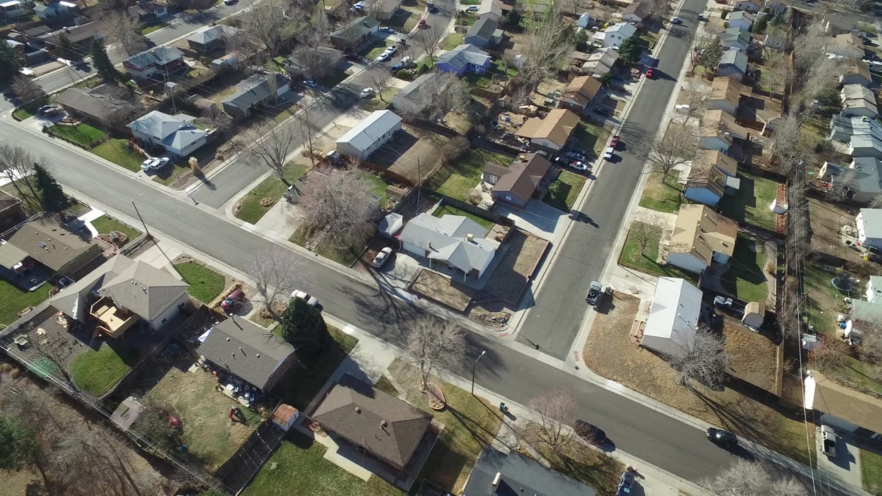 Drone-height view over Hidden Lake, Colorado residential blocks, showing a diagonal road, light and dark rooftops, lawns, driveways, and no visible people.