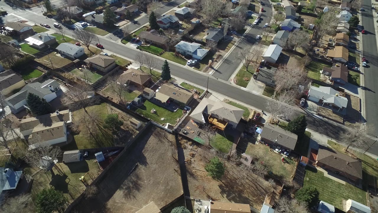 Aerial view in Hidden Lake, Colorado with rooftops, backyard fences, a curving residential road at the lower right, parked vehicles, winter-bare trees, and no visible people.