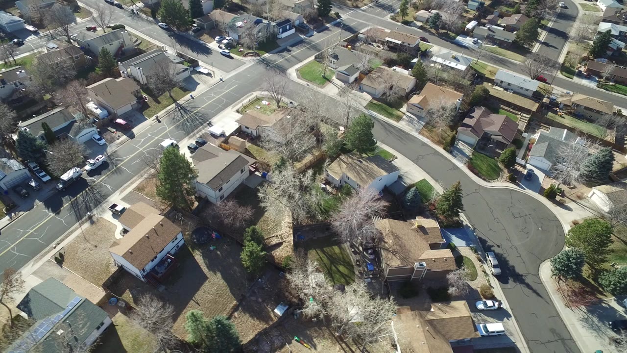 Aerial view of suburban houses, streets, cars, and leafless trees.