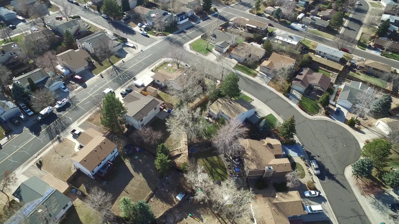 Aerial frame of Hidden Lake, Colorado showing a curved residential road, detached houses, parked vehicles, bare trees, and sunlit yards.