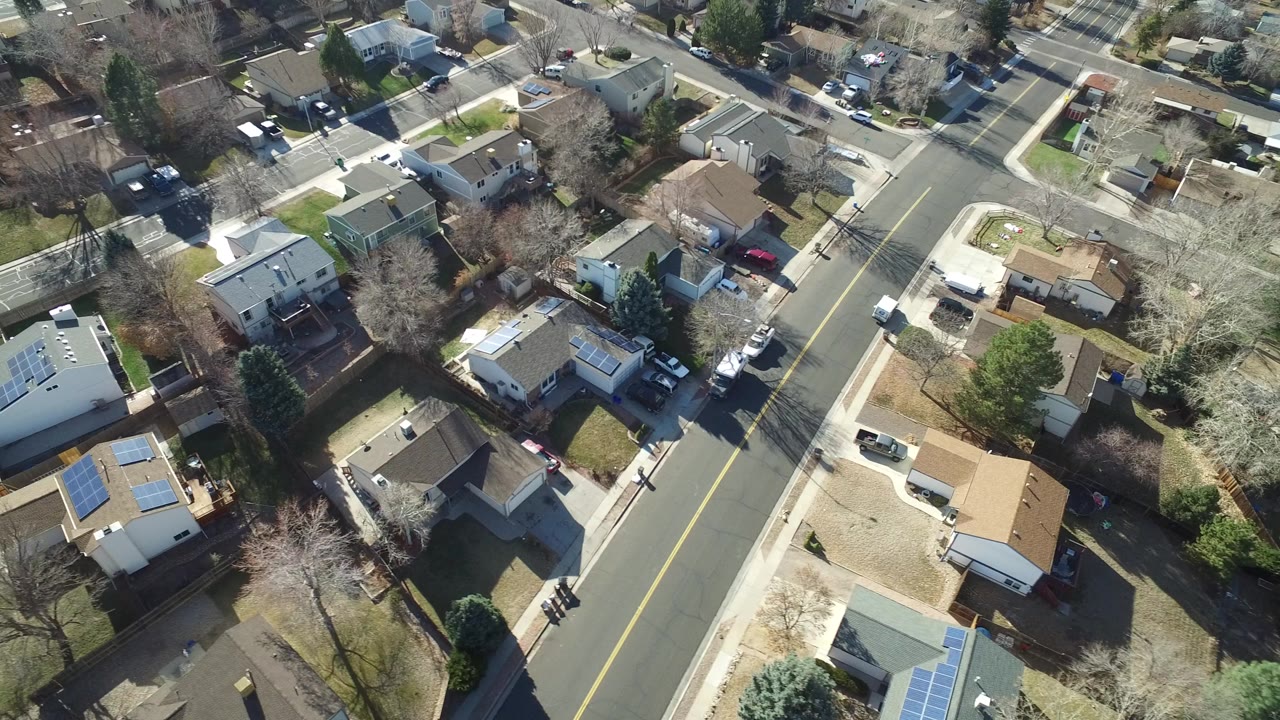 Oblique aerial view over Hidden Lake, Colorado homes, a curved residential street, parked cars, bare trees, green yards, and no visible people.