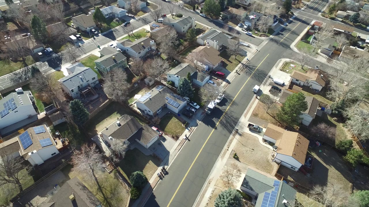 Aerial frame over Hidden Lake, Colorado showing a two-lane road, intersecting side streets, residential roofs, winter-bare trees, lawns, and no visible people.