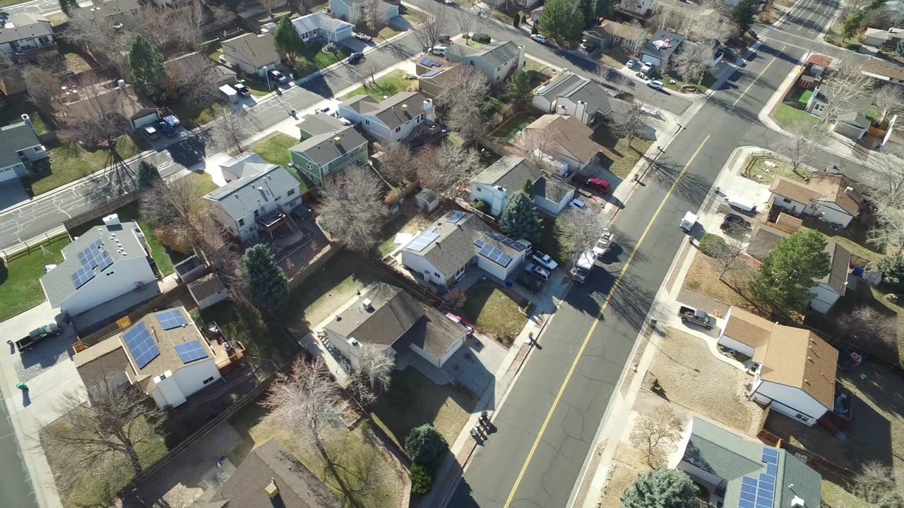 Drone-like view of houses, a road junction, lawns, and rooftops.
