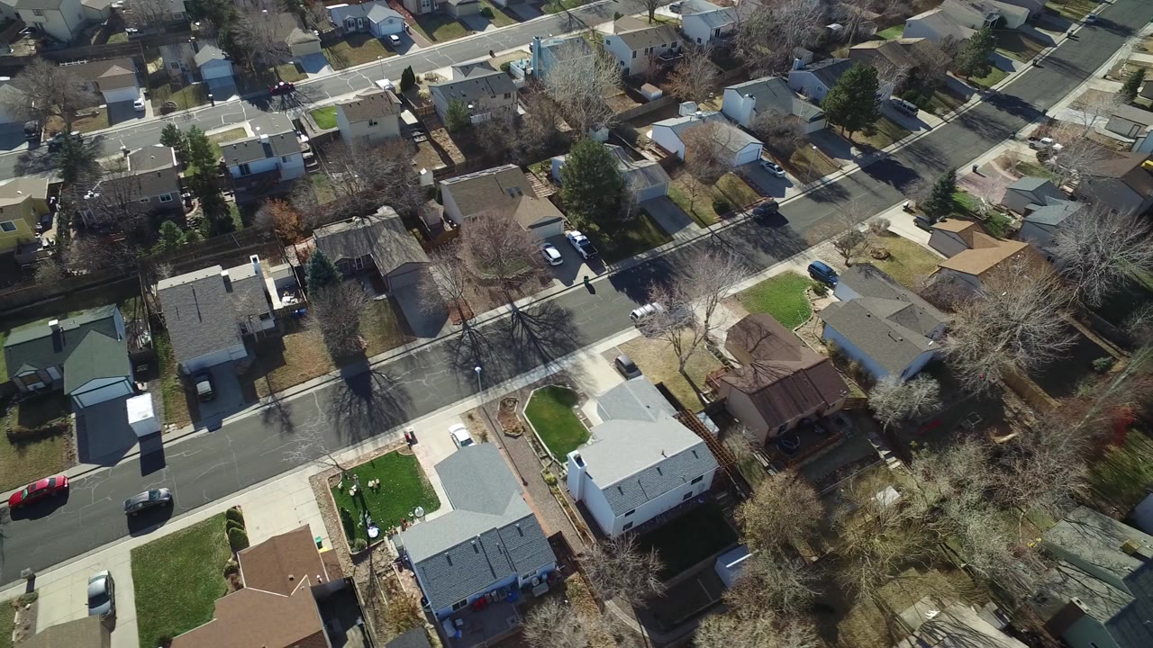 Aerial view over suburban houses, streets, yards, and parked cars.