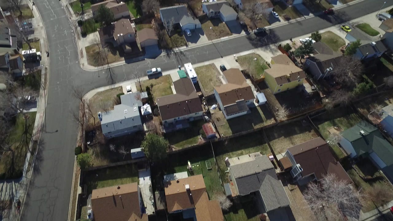 Aerial frame over Hidden Lake, Colorado homes with rooftops, fenced yards, driveways, leafless trees, and a curved residential street, with no visible people.