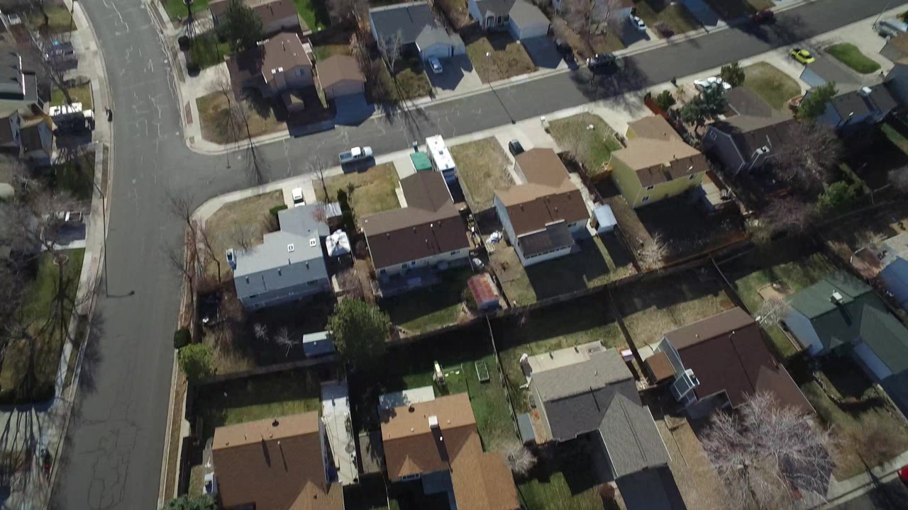 Aerial view in Hidden Lake, Colorado showing a row of houses, backyard fences, a broad street at left, pale winter lawns, and no visible people.