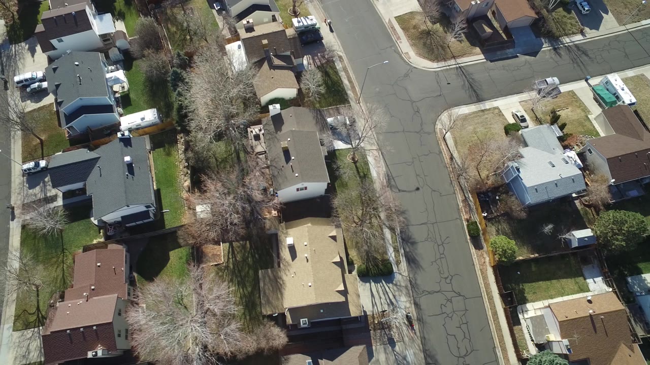 Aerial frame over Hidden Lake, Colorado with rooftops, fenced backyards, an asphalt intersection, sidewalks, and no visible people.