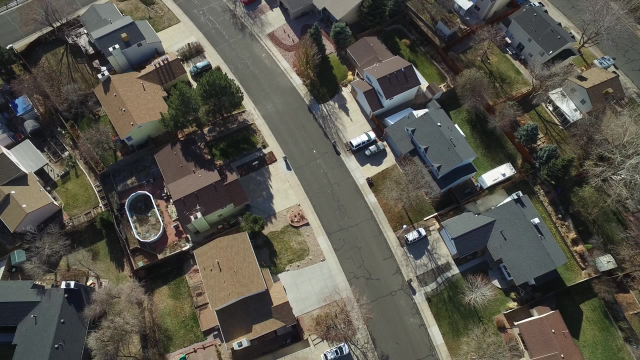 Top-down residential block with houses, trees, and parked vehicles.