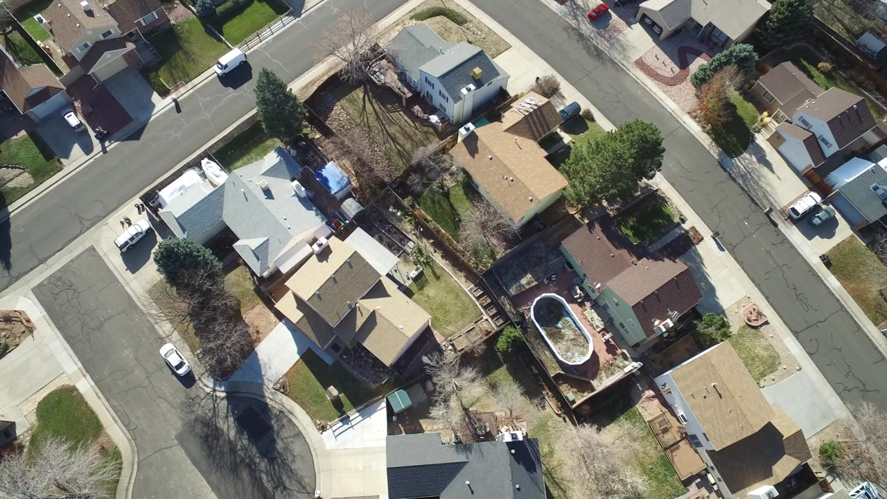 Top-down aerial frame over Hidden Lake, Colorado showing a residential intersection, rooftops, driveways, fenced yards, parked vehicles, and no visible people.