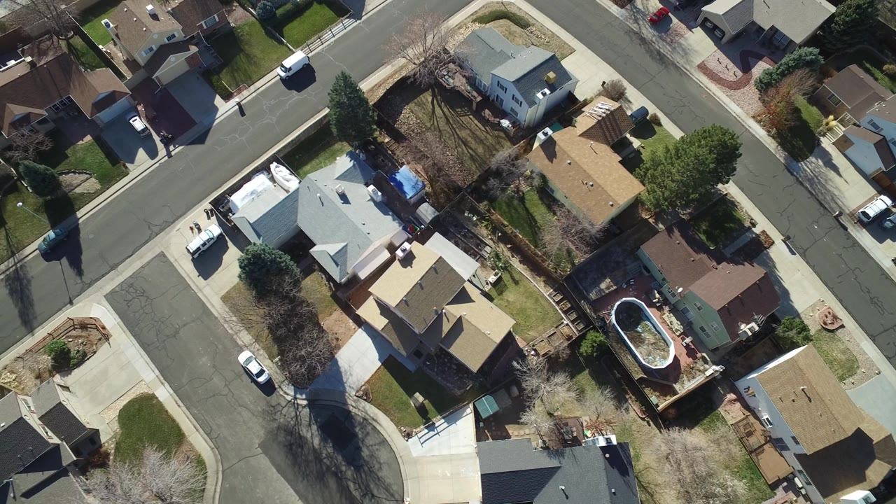 Overhead Hidden Lake, Colorado frame showing tan and gray rooftops, backyards, a white vehicle on the street, long tree shadows, and no visible people.