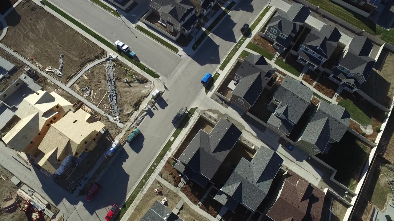Overhead view of new houses, streets, dirt lots, and a framed house under construction.
