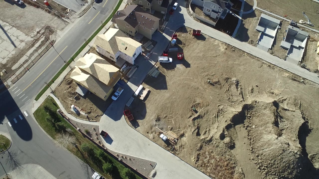 Top-down aerial frame over Hidden Lake, Colorado showing unfinished wood-framed homes beside a curved road, dirt construction lots, parked trucks, and no clearly visible people.