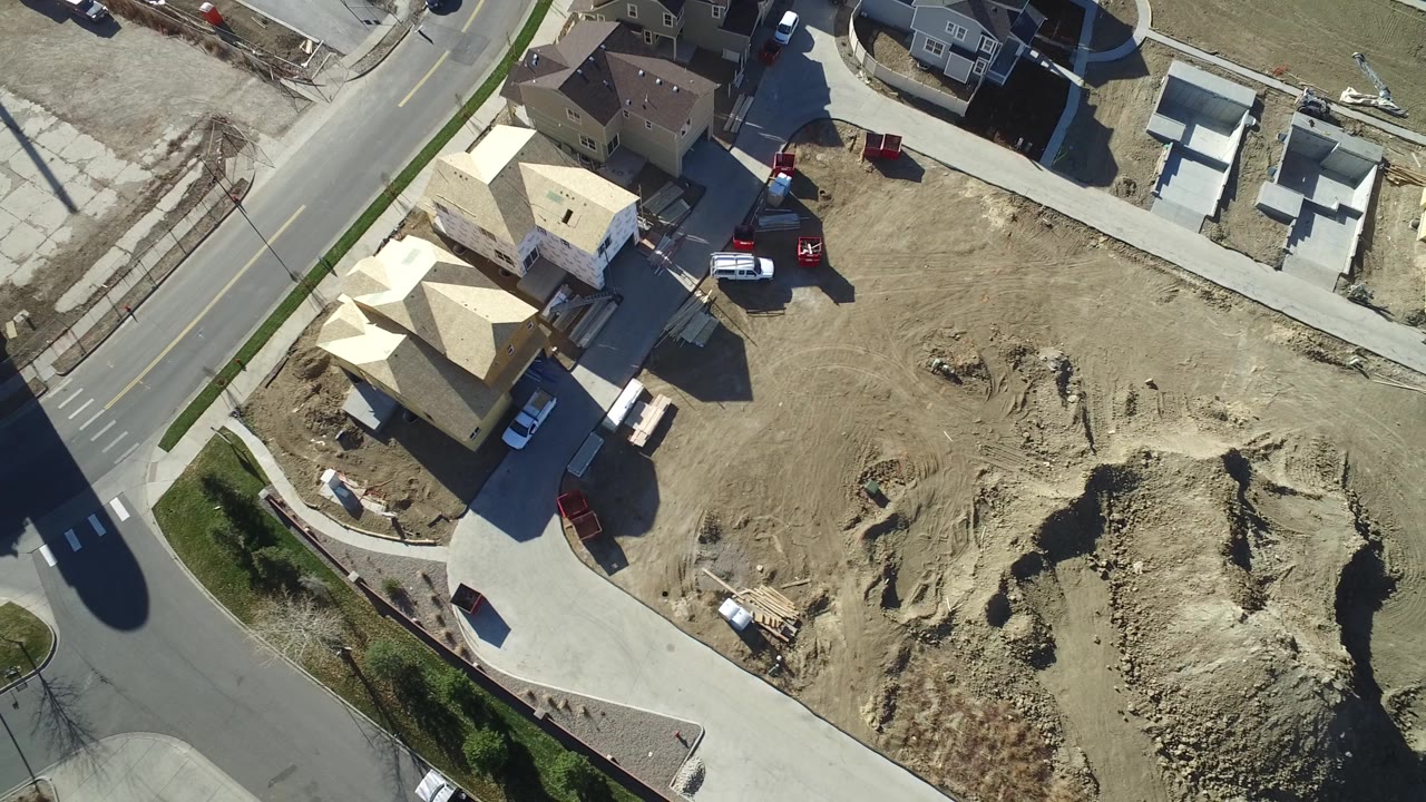Aerial view in Hidden Lake, Colorado with framed residential structures at left, open dirt grading in the center, parked vehicles, and subdivision streets around the lot.