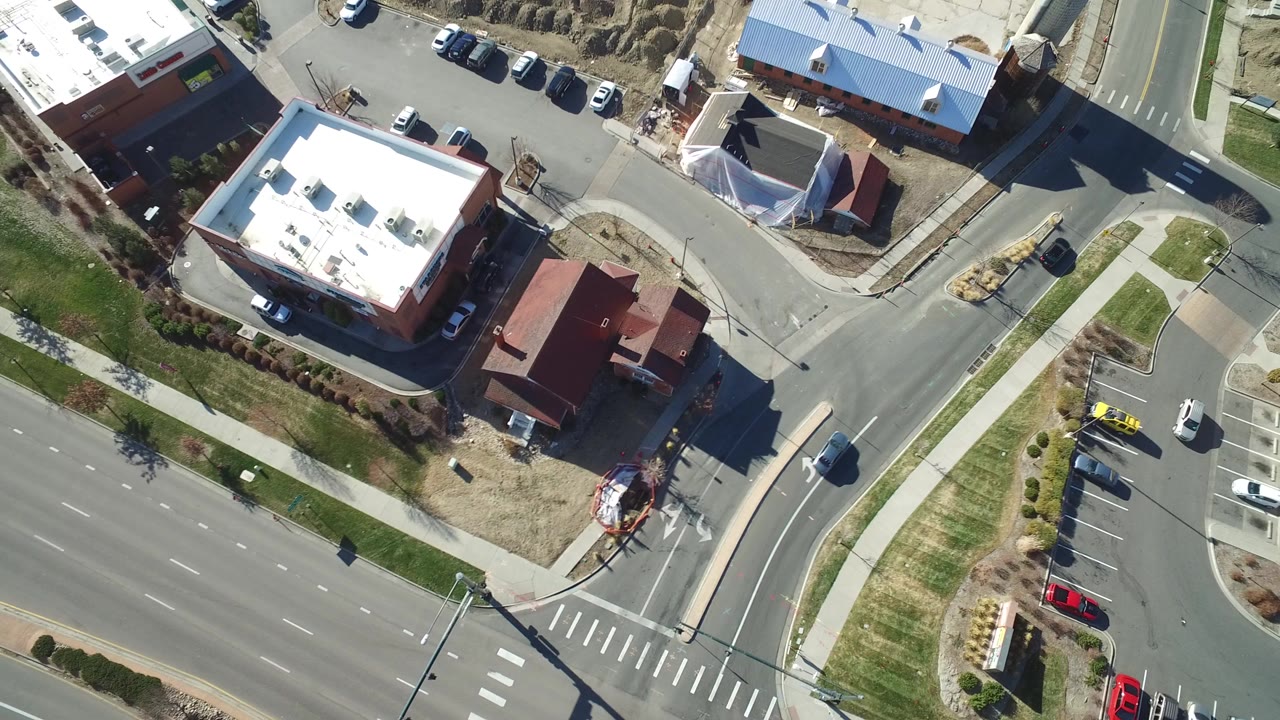 High aerial frame over Hidden Lake, Colorado showing a broad multilane roadway, a corner junction, sidewalks, low buildings, parked cars, and no visible people.