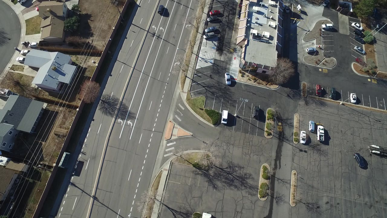 Overhead view of a multi-lane road beside houses and parking lots.