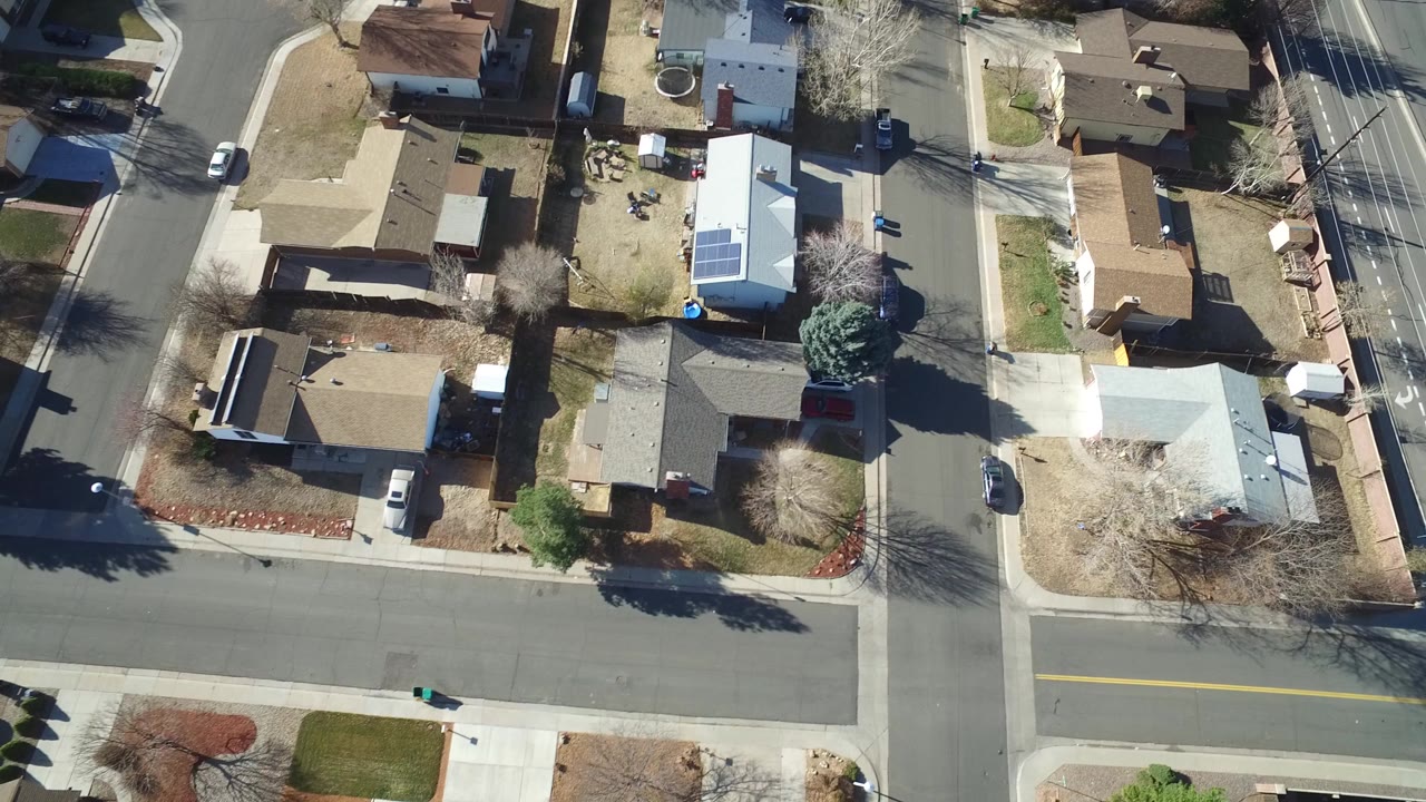 High aerial frame over Hidden Lake, Colorado homes, with an intersection, driveways, bare trees, parked cars, and no visible people.