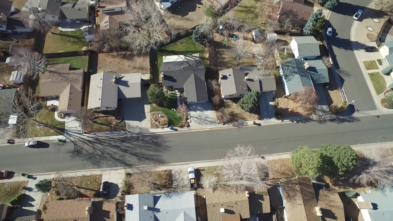 Overhead aerial frame of Hidden Lake, Colorado homes along a paved street, with rooftops, driveways, bare trees, lawns, parked cars, and no visible people.