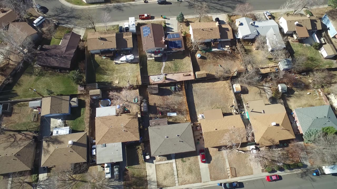 A high drone view over Hidden Lake, Colorado shows a row of houses, backyard fences, parked cars along the street, and no visible people one second into the clip.