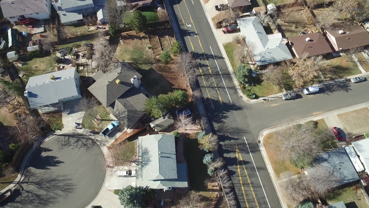 Overhead frame in Hidden Lake, Colorado with the cul-de-sac centered lower left, an intersecting residential street, parked vehicles, detached houses, and winter-bare trees casting long shadows.
