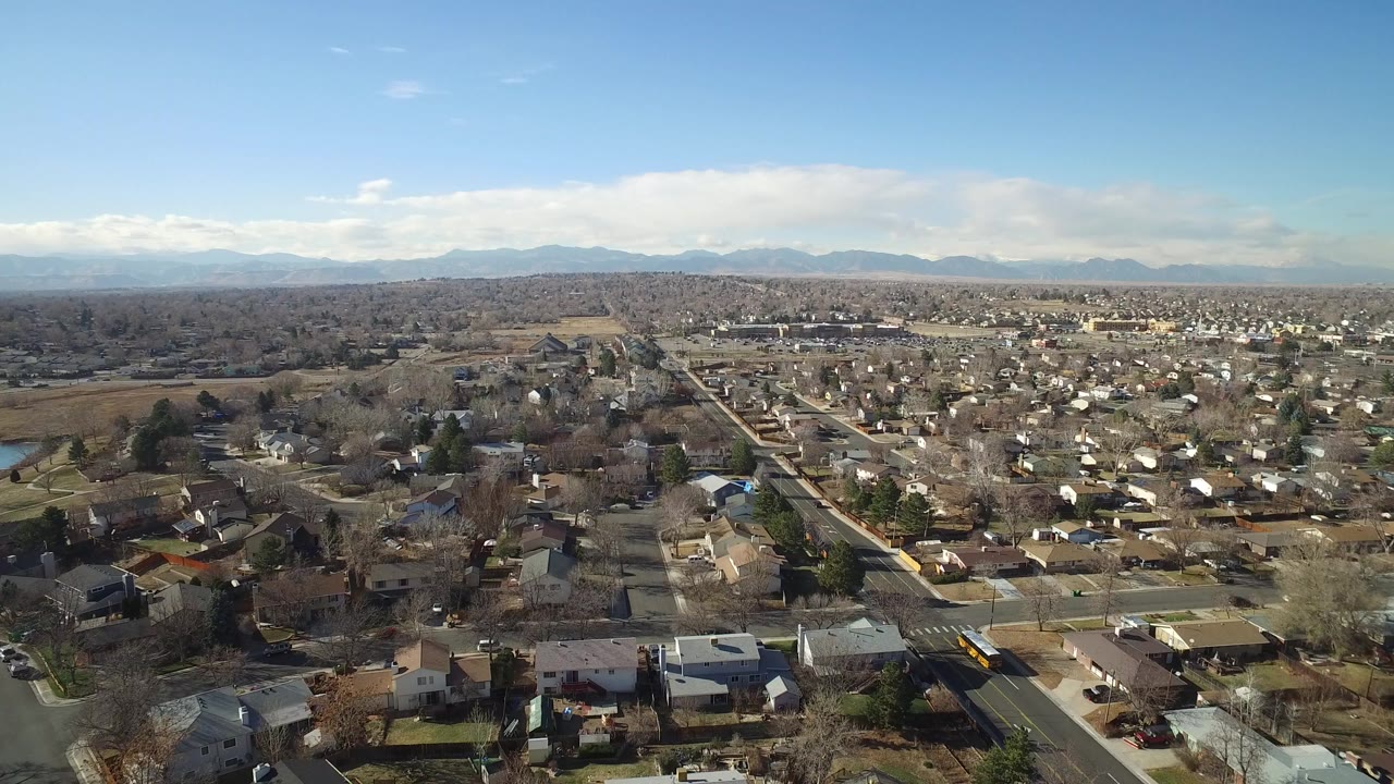 Aerial view over suburban houses, streets, trees, and distant mountains.