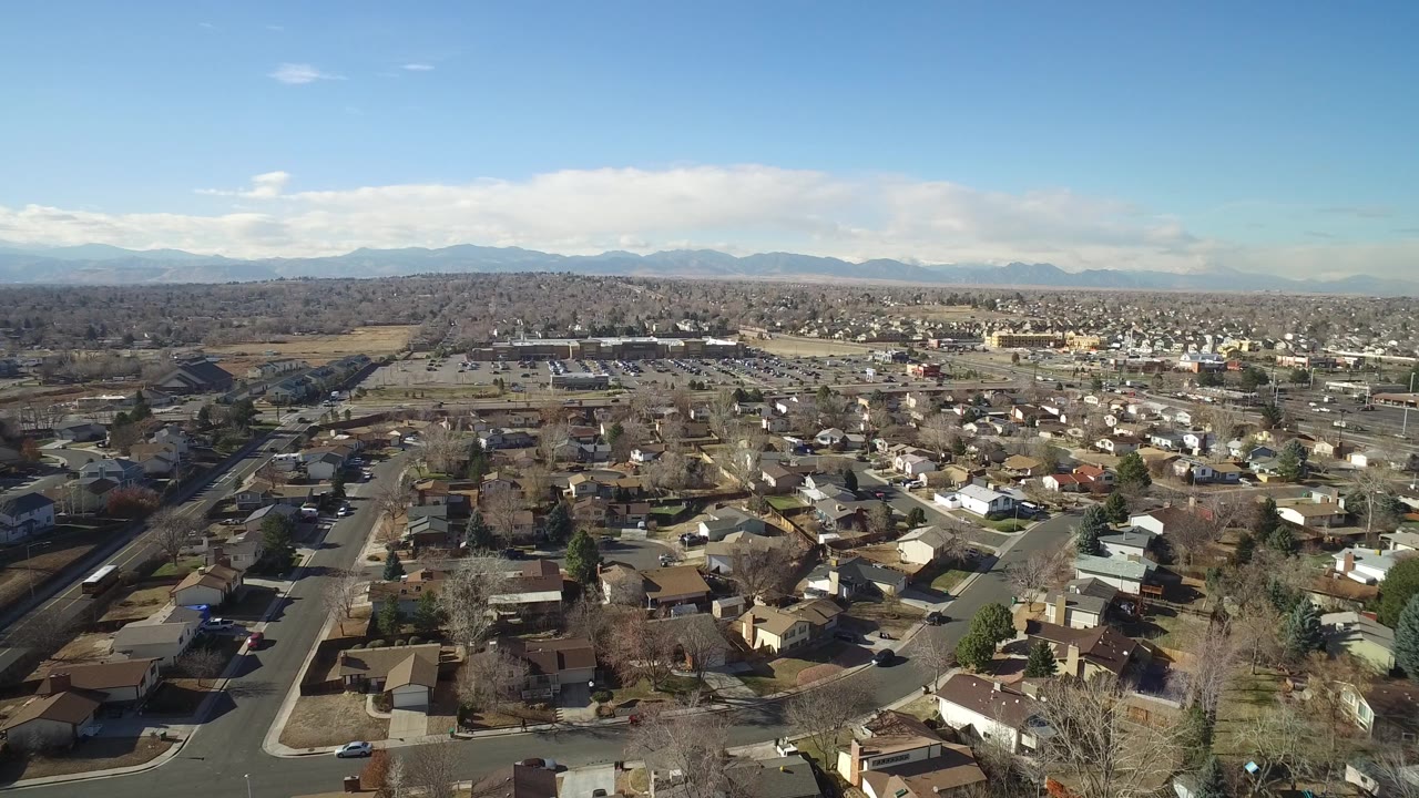 A high aerial view across Hidden Lake, Colorado shows rows of modest houses, a road corridor at left, open ground beyond the homes, and mountains along the horizon, with no recognizable people visible.