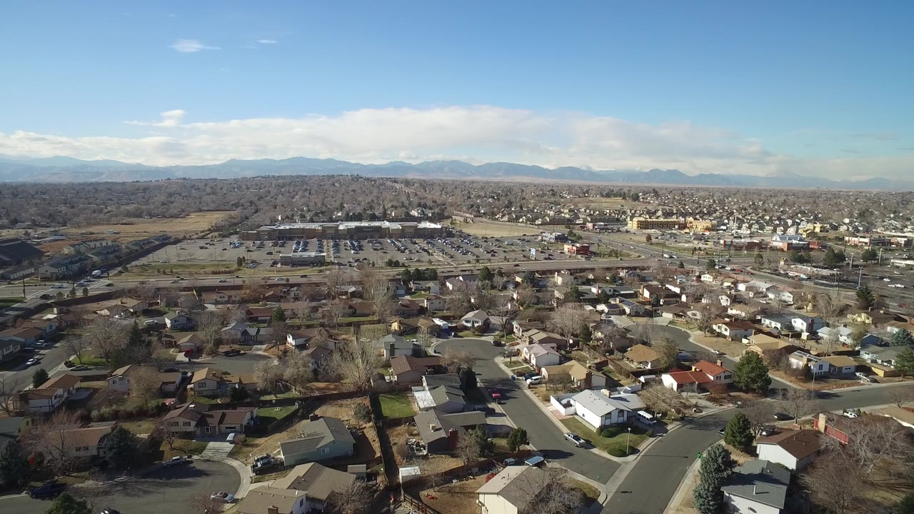 Suburban rooftops and streets seen from above with a commercial strip and mountains beyond.