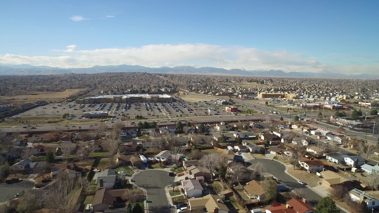 Aerial view over suburban homes, roads, parking lots, and distant mountains.